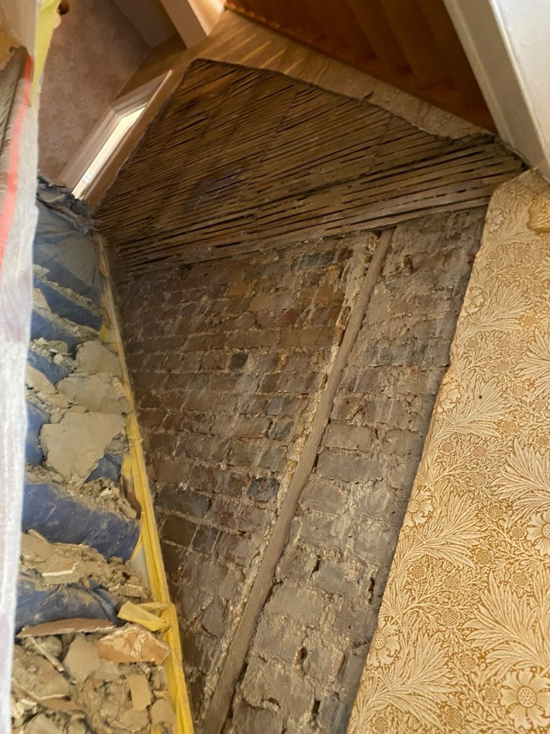 Stairwell wall stripped to brick and lath, before